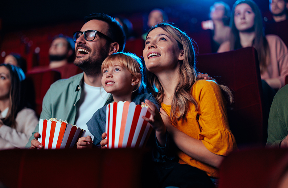 A Family enjoying a popcorn in a theatre and enjoying a movie.